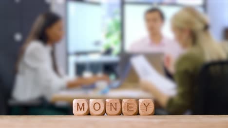 Business-Concept-Wooden-Letter-Cubes-Or-Dice-Spelling-Money-With-Office-Meeting-In-Background