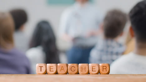 Education-Concept-With-Wooden-Letter-Cubes-Or-Dice-Spelling-Teacher-With-Student-Lecture-In-Background