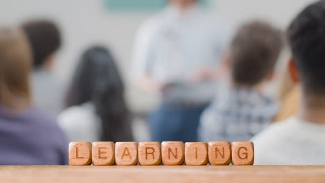 Education-Concept-With-Wooden-Letter-Cubes-Or-Dice-Spelling-Learning-With-Student-Lecture-In-Background