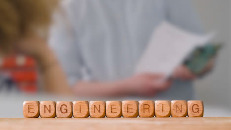 Education-Concept-With-Wooden-Letter-Cubes-Or-Dice-Spelling-Engineering-With-Students-Meeting-In-Background