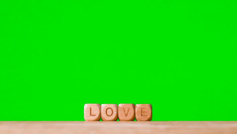Concept-With-Wooden-Letter-Cubes-Or-Dice-Spelling-Love-Against-Green-Screen