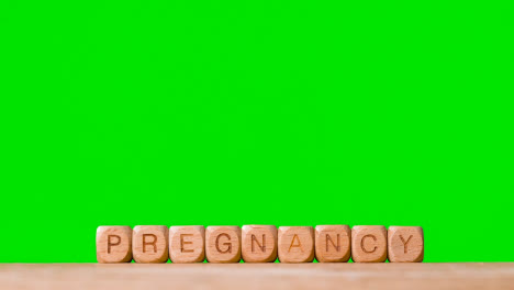 Concept-With-Wooden-Letter-Cubes-Or-Dice-Spelling-Pregnancy-Against-Green-Screen-Background