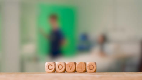 Medical-Concept-With-Wooden-Letter-Cubes-Or-Dice-Spelling-Covid-Against-Background-Of-Nurse-Talking-To-Patient-In-Hospital-Bed