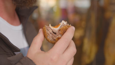 Close-Up-Of-Man-Eating-Scotch-Egg-From-Takeaway-Food-Stall-In-Borough-Market-London-UK