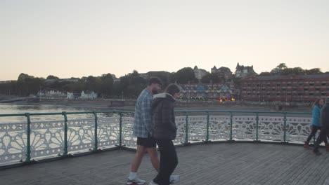 People-Walking-Along-Penarth-Pier-In-Wales-Towards-Town-At-Dusk