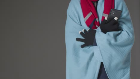 Nahaufnahme-Einer-Person,-Die-Decke-Und-Handschuhe-Trägt-Und-Mit-Dem-Handy-Versucht,-Sich-In-Der-Energiekrise-Warm-Zu-Halten-1