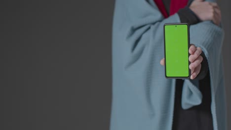 Close-Up-Of-Cold-Person-Wearing-Blanket-Holding-Green-Screen-Mobile-Phone-Trying-To-Keep-Warm-In-Energy-Crisis