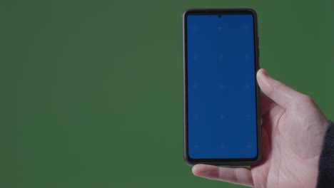 Nahaufnahme-Einer-Person,-Die-Ein-Handy-Mit-Blauem-Bildschirm-Vor-Grünem-Hintergrund-Hält-1