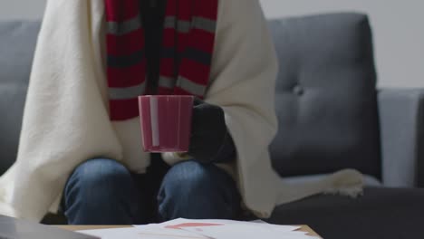Person-Wearing-Blanket-With-Hot-Drink-Sitting-On-Sofa-At-Home-Trying-To-Keep-Warm-In-Energy-Crisis-3