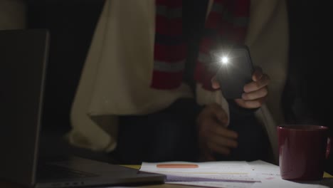 Person-Wearing-Blanket-Sitting-On-Sofa-At-Home-In-Dark-When-Power-Is-Cut-Off-Using-Phone-Torch