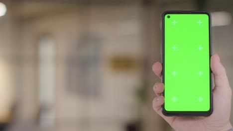 Close-Up-Of-Person-At-Home-Holding-Green-Screen-Mobile-Phone-In-Lounge