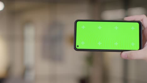 Close-Up-Of-Person-At-Home-Holding-Green-Screen-Mobile-Phone-In-Lounge-1