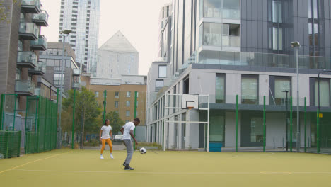 Artificial-Soccer-Pitch-In-Urban-City-Area-With-Young-Couple-Kicking-Football-