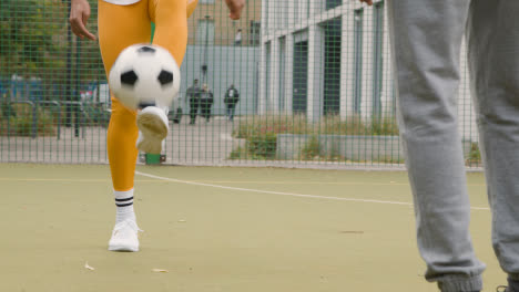 Close-Up-Of-Artificial-Soccer-Pitch-In-Urban-City-Area-With-Young-Couple-Kicking-Football-
