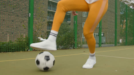 Close-Up-Of-Woman-Dribbling-Football-Past-Man-On-Artificial-Soccer-Pitch-In-Urban-City-Area-