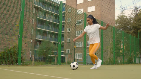 Football-Female-Player-Dribbling-Ball-On-Artificial-Soccer-Pitch-In-Urban-City-Area-1