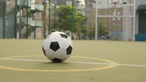 View-Of-Football-On-Centre-Circle-On-Empty-Artificial-Soccer-Pitch-In-Urban-City-Area-