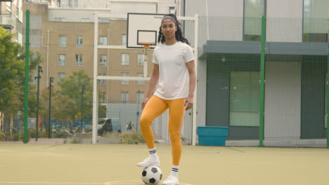Portrait-Of-Young-Woman-With-Football-On-Artificial-Soccer-Pitch-In-Urban-City-Area-