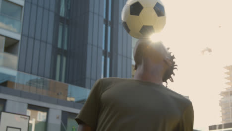 Male-Football-Player-Practising-Ball-Control-On-Artificial-Soccer-Pitch-In-Urban-City-Area-Balancing-Football-On-Head