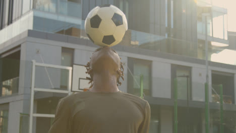 Male-Football-Player-Practising-Ball-Control-On-Artificial-Soccer-Pitch-In-Urban-City-Area-Balancing-Football-On-Head-1