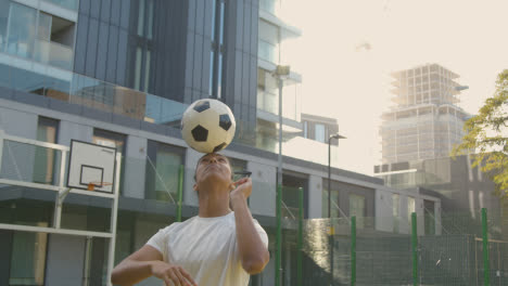 Female-Football-Player-Practising-Ball-Control-On-Artificial-Soccer-Pitch-In-Urban-City-Area-Balancing-Football-On-Head-1