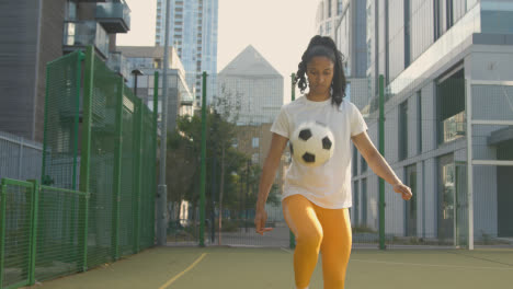 Female-Football-Player-Practising-Ball-Control-On-Artificial-Soccer-Pitch-In-Urban-City-Area