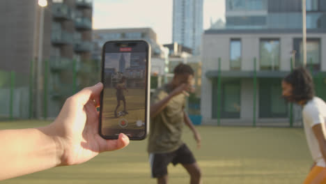 Person-Filming-Players-Kicking-And-Passing-Football-On-Artificial-Soccer-Pitch-In-Urban-City-Area-On-Mobile