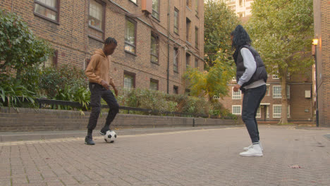 Young-Couple-Kicking-And-Passing-Football-Walking-Along-Street-In-Urban-City-Area-1