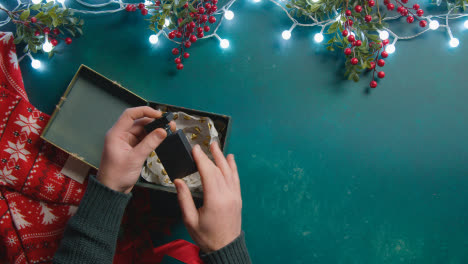 Fotografía-Cenital-De-Una-Persona-Con-Adornos-Navideños-Abriendo-Un-Regalo-De-Perfume