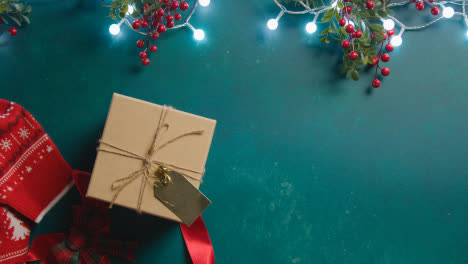 Overhead-Schuss-Von-Weihnachtsbeleuchtung-Mit-Beeren-Und-Geschenk-Verpackt-Auf-Grünem-Hintergrund