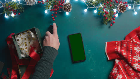 Overhead-Shot-Of-Person-With-Green-Screen-Mobile-Phone-With-Christmas-Decorations-And-Gift-Of-Perfume-1