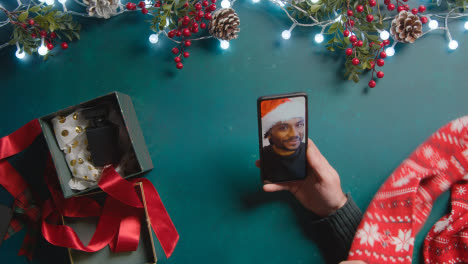 Fotografía-Cenital-De-Una-Persona-Que-Tiene-Una-Videollamada-Navideña-Con-Un-Amigo-En-Un-Teléfono-Móvil-Con-Adornos-Navideños-Como-Fondo