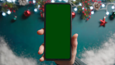 Overhead-Shot-Of-Person-Holding-Green-Screen-Mobile-Phone-Above-Christmas-Decorations-2