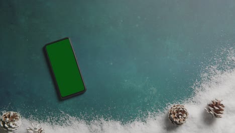 Overhead-Shot-Of-Person-With-Green-Screen-Mobile-Phone-Above-Christmas-Background