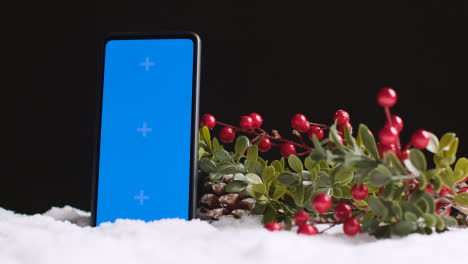 Blue-Screen-Mobile-Phone-On-Christmas-Background-With-Snow-And-Foliage-3