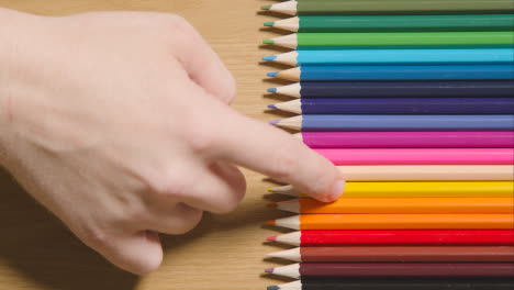 Lápices-De-Colores-Dispuestos-En-Una-Línea-Sobre-Fondo-De-Madera-Con-Una-Persona-Que-Elige-Uno-Amarillo