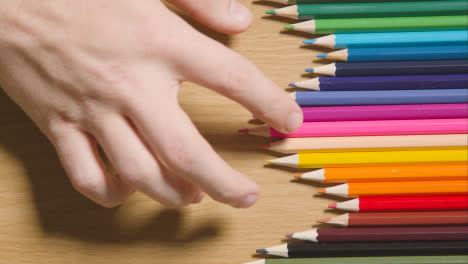 Lápices-De-Colores-Dispuestos-En-Una-Línea-Sobre-Fondo-De-Madera-Con-Una-Persona-Que-Elige-Rosa