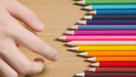 Lápices-De-Colores-Dispuestos-En-Una-Línea-Sobre-Fondo-De-Madera-Con-Una-Persona-Que-Elige-Rosa-1