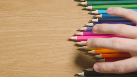 Lápices-De-Colores-Dispuestos-En-Una-Línea-Sobre-Fondo-De-Madera-Con-Una-Persona-Que-Elige-Rosa-2