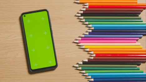 Coloured-Pencils-In-A-Line-On-Wooden-Background-With-Person-Choosing-Pink-One-And-Green-Screen-Mobile-Phone