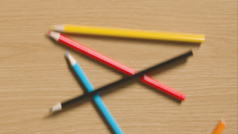Mehrfarbige-Bleistifte,-Die-Hölzernen-Hintergrund-Hinunterrollen