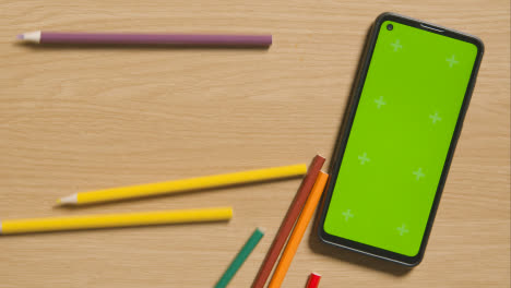 Mehrfarbige-Stifte-Rollen-Neben-Dem-Handy-Mit-Grünem-Bildschirm-Auf-Holzhintergrund