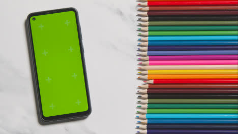 Coloured-Pencils-In-A-Line-On-Marble-Background-With-Person-Replacing-Red-One-And-Green-Screen-Mobile-Phone