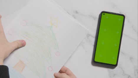 Overhead-Shot-Of-Child-With-Coloured-Pencils-And-Drawing-And-Green-Screen-Phone-On-Marble-Background