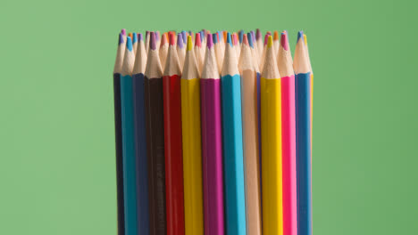 Studio-Shot-Of-Rotating-Multi-Coloured-Pencils-Against-Green-Background