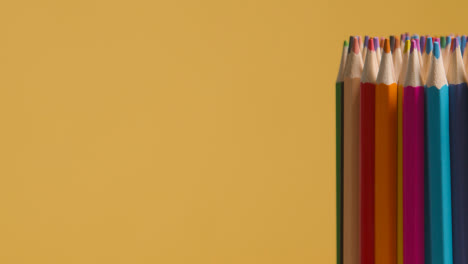 Studio-Shot-Of-Rotating-Multi-Coloured-Pencils-Against-Yellow-Background-1
