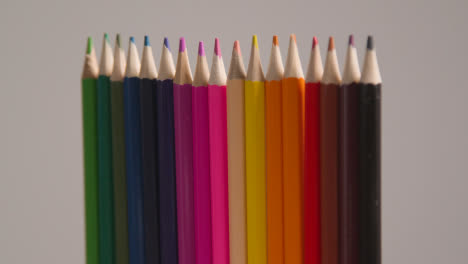 Studio-Shot-Of-Rotating-Line-Of-Multi-Coloured-Pencils-Against-Grey-Background-