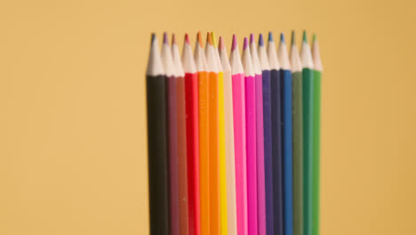 Studio-Shot-Of-Rotating-Line-Of-Multi-Coloured-Pencils-Against-Yellow-Background-1