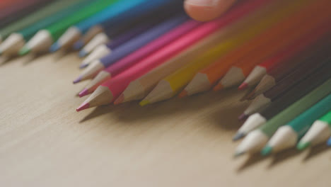Lápices-De-Colores-En-Una-Línea-Sobre-Fondo-De-Madera-Con-Una-Persona-Que-Elige-Rosa-2