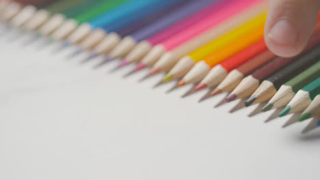 Studio-Shot-Of-Multi-Coloured-Pencils-In-A-Line-On-White-Background-With-Hand-Choosing